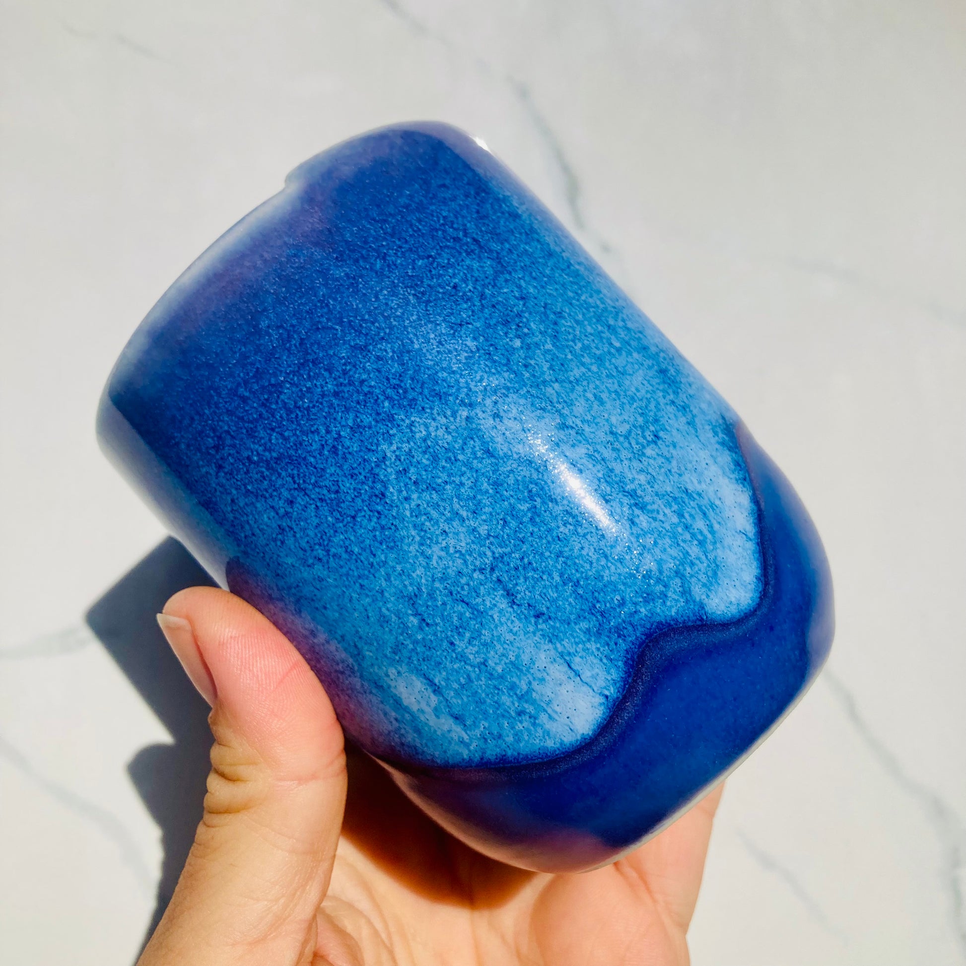 Close-up of indigo blue handmade ceramic travel mug with drippy glaze and dimple grip